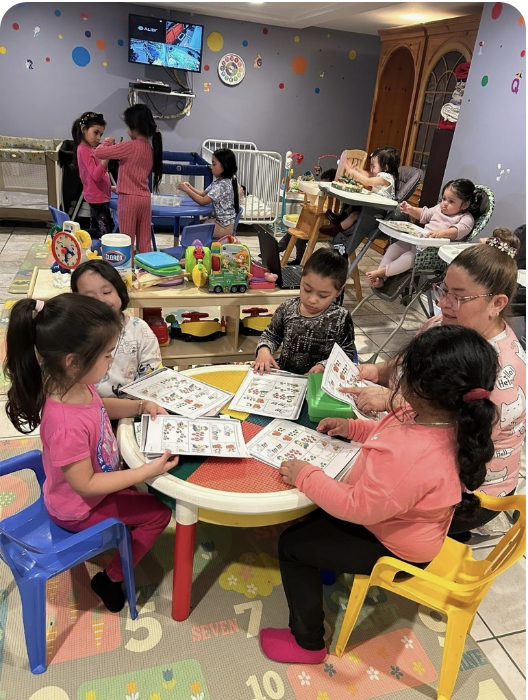 Children and caregivers sharing learning activities around a table at Miriam Daycare
